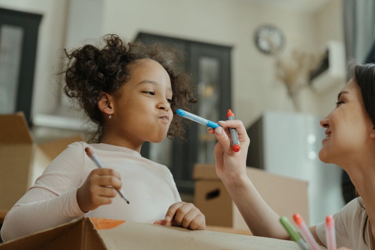 A joyful moment of mother and daughter drawing together surrounded by moving boxes.