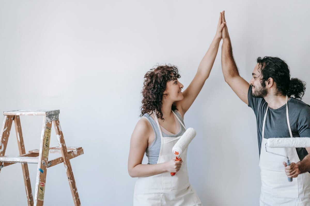 A joyful couple high-fiving during a home painting project, expressing teamwork and success.